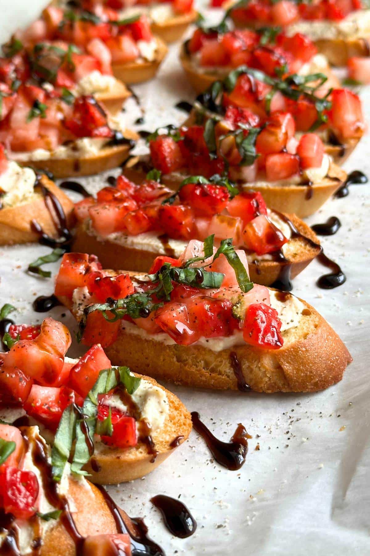 Strawberry balsamic crostini with basil and tofu ricotta in a line on a sheet of parchment paper.