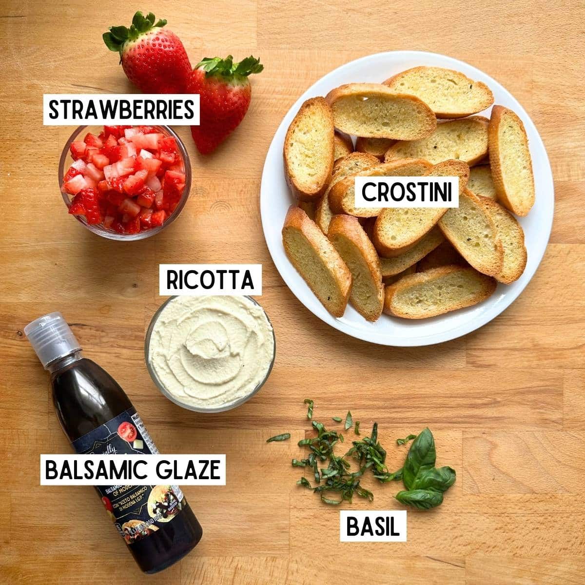 Ingredients needed to make strawberry crostini with corresponding labels: strawberries, crostini, ricotta, balsamic glaze, and basil.