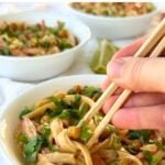 Vegan Thai peanut noodle salad in a bowl cilantro and green onions on top and a pair of chopsticks digging in.