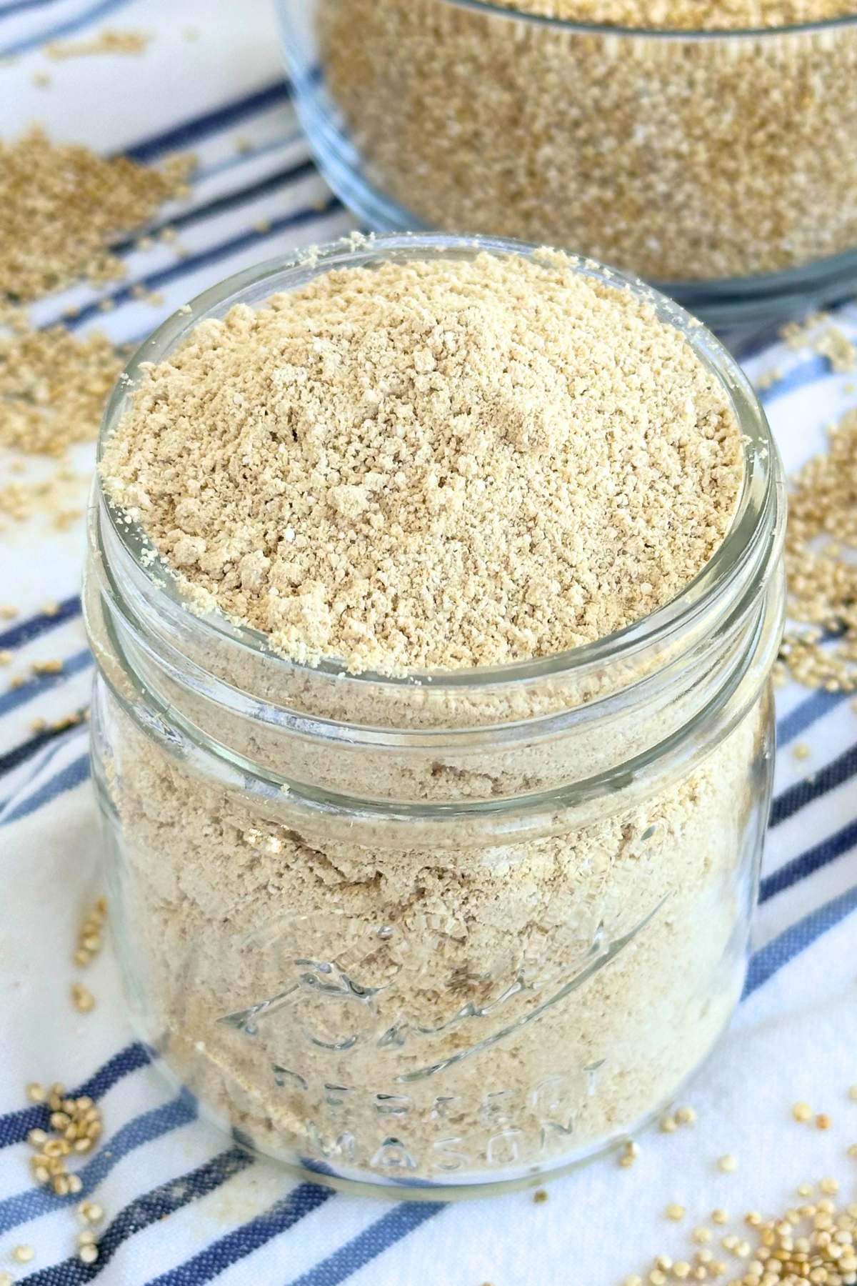 Quinoa flour in a small mason jar with whole quinoa seeds in the background.