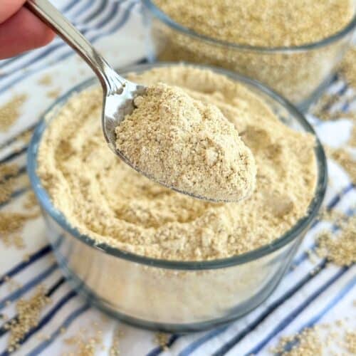 Homemade quinoa flour on a spoon with more in the background in a bowl and another bowl with whole quinoa seeds.