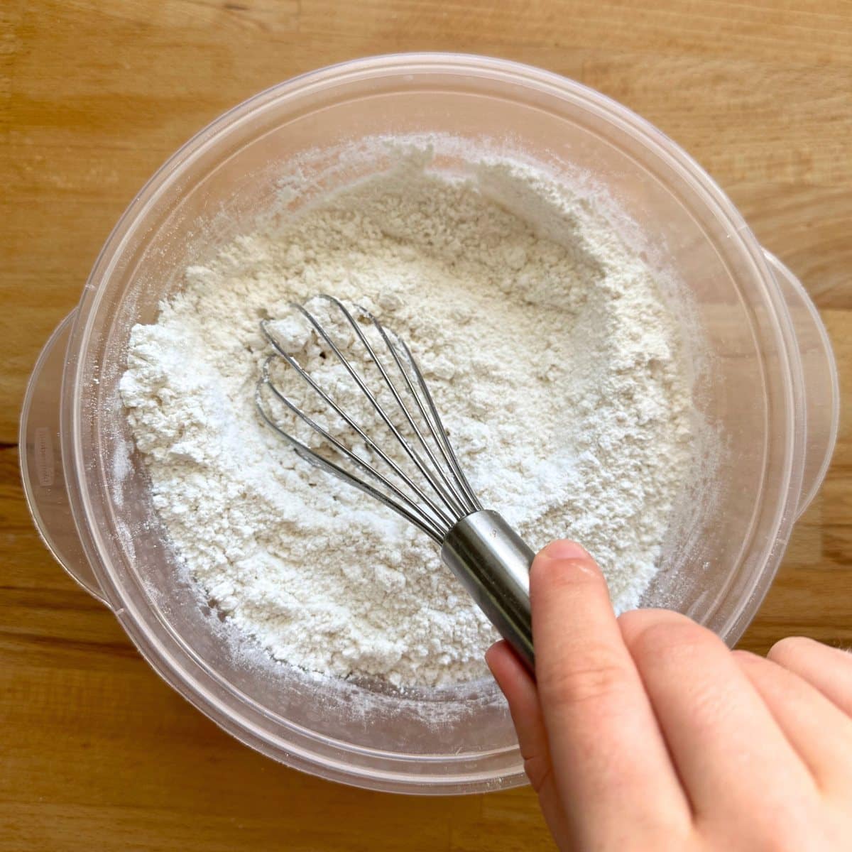 Whisking dry ingredients with a whisk in a clear bowl.