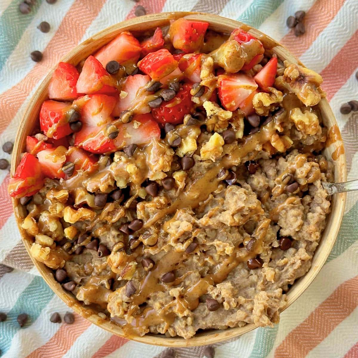 Protein steel cut oats in a bowl, topped with chopped strawberries, walnuts, chocolate chips, and almond butter.