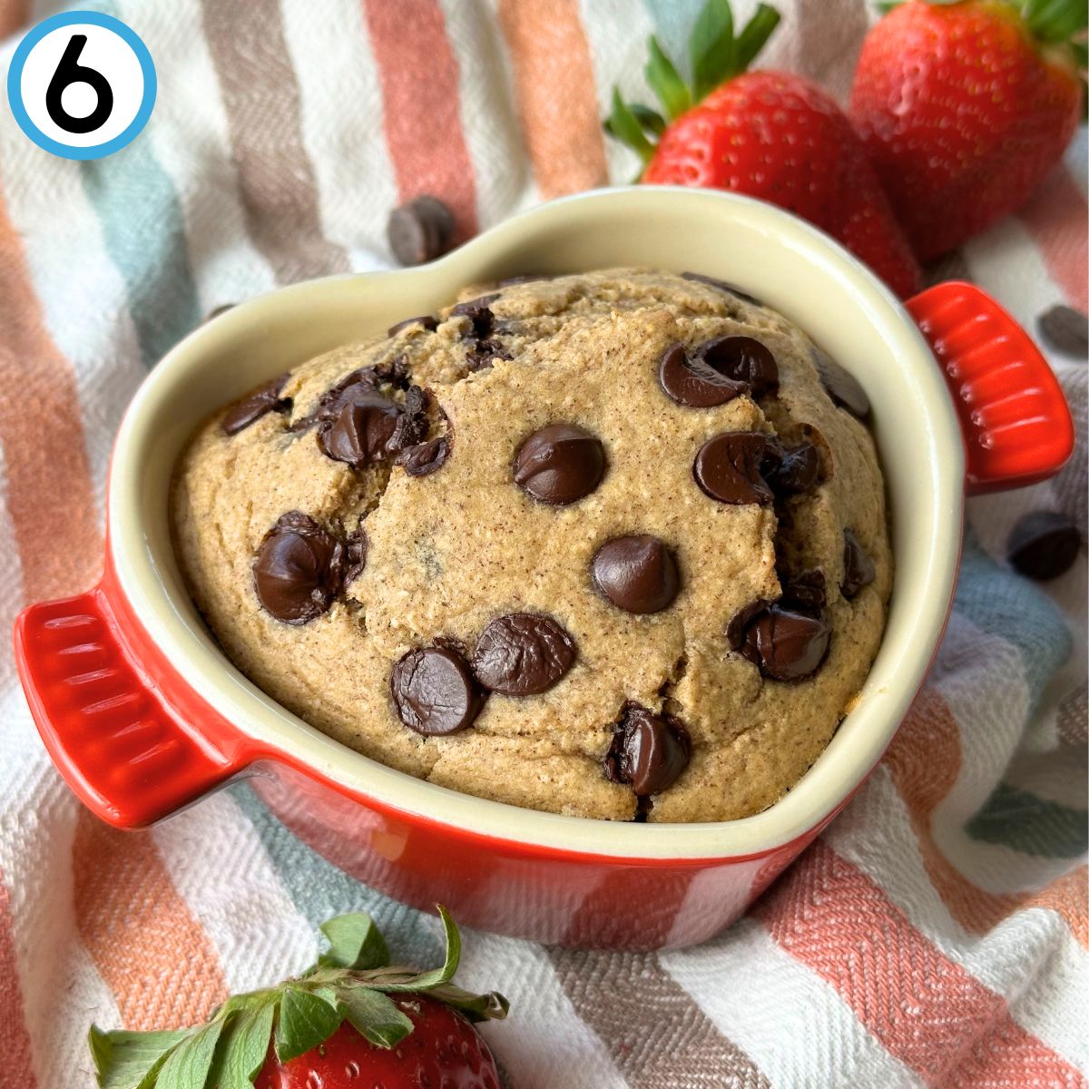 Baked oatmeal in a heart shaped ramekin with chocolate chips and strawberries in the background.