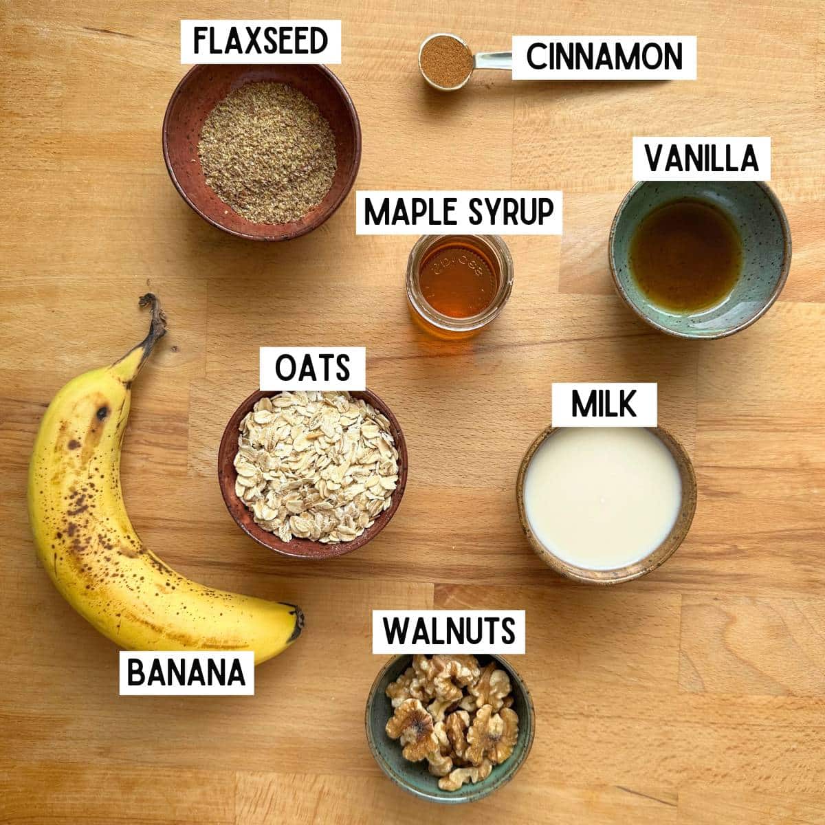 Ingredients needed to make banana bread overnight oats with corresponding labels: flaxseed, cinnamon, maple syrup, vanilla, banana, oats, milk, and walnuts.