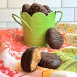 Chocolate almond butter egg with a bite taken out of it resting on top of another chocolate egg; more chocolate eggs are in a green basket in the background on top of a floral napkin.