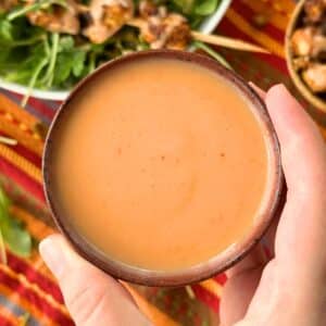 Vegan bang bang sauce, light orange in color, in a bowl being held by a hand with bang bang tofu in the background.