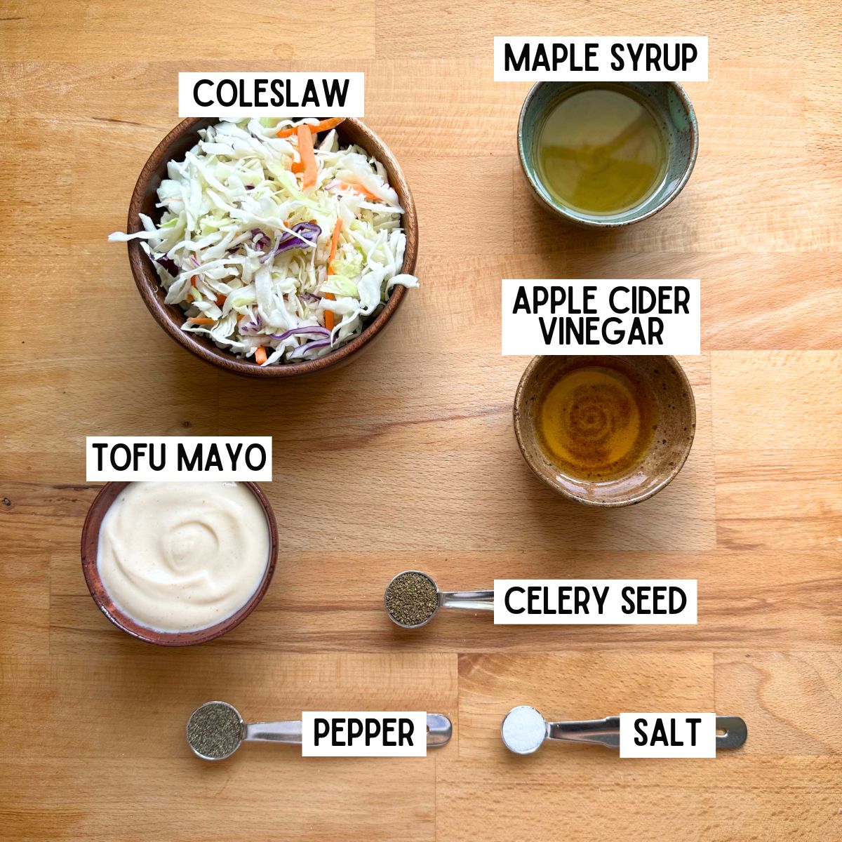 Ingredients needed to make vegan coleslaw with corresponding labels: coleslaw, maple syrup, apple cider vinegar, tofu mayo, celery seed, pepper, and salt.