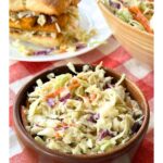 Bowl of creamy vegan coleslaw in a wooden bowl on a checkered red and white napkin.