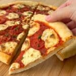 Slice of vegan pizza with a fluffy gluten-free crust, more pizza is in the background.