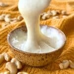 Stretchy vegan cashew mozzarella cheese being stretched from a bowl by a spoon.