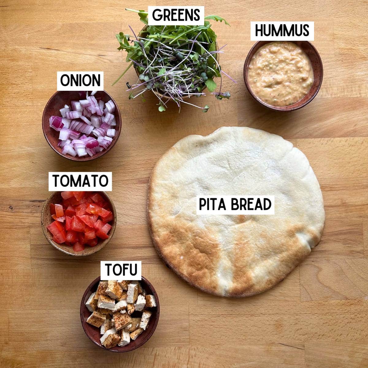 Ingredients with labels: hummus, greens, onion, tomato, tofu, and pita bread.