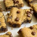 Square piece of a chickpea blondie with a bite taken out of it surrounding by more blondies with chocolate chips.