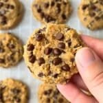 Chickpea cookie with chocolate chips being held with more in the background on parchment paper.