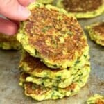 Stack of crispy vegan zucchini fritters with one being lifted up.