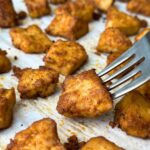 Crispy, golden BBQ tofu nugget on a fork with more on a baking sheet.