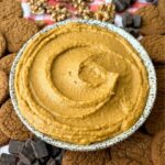 Bowl of pumpkin pie hummus with a swirl in it, ginger snaps, chocolate chips, and walnuts are in the background.