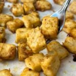 Maple dijon tofu cubes on a fork with more on a baking tray.