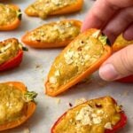 Hand picking up a cheesy mini bell pepper popper with more on a baking sheet.