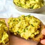 Vegan egg salad on a piece of toast with a bowl of eggless egg salad in the background.