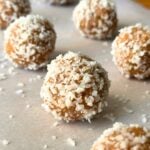 Coconut date balls on a sheet of parchment paper with a few pieces of shredded coconut.