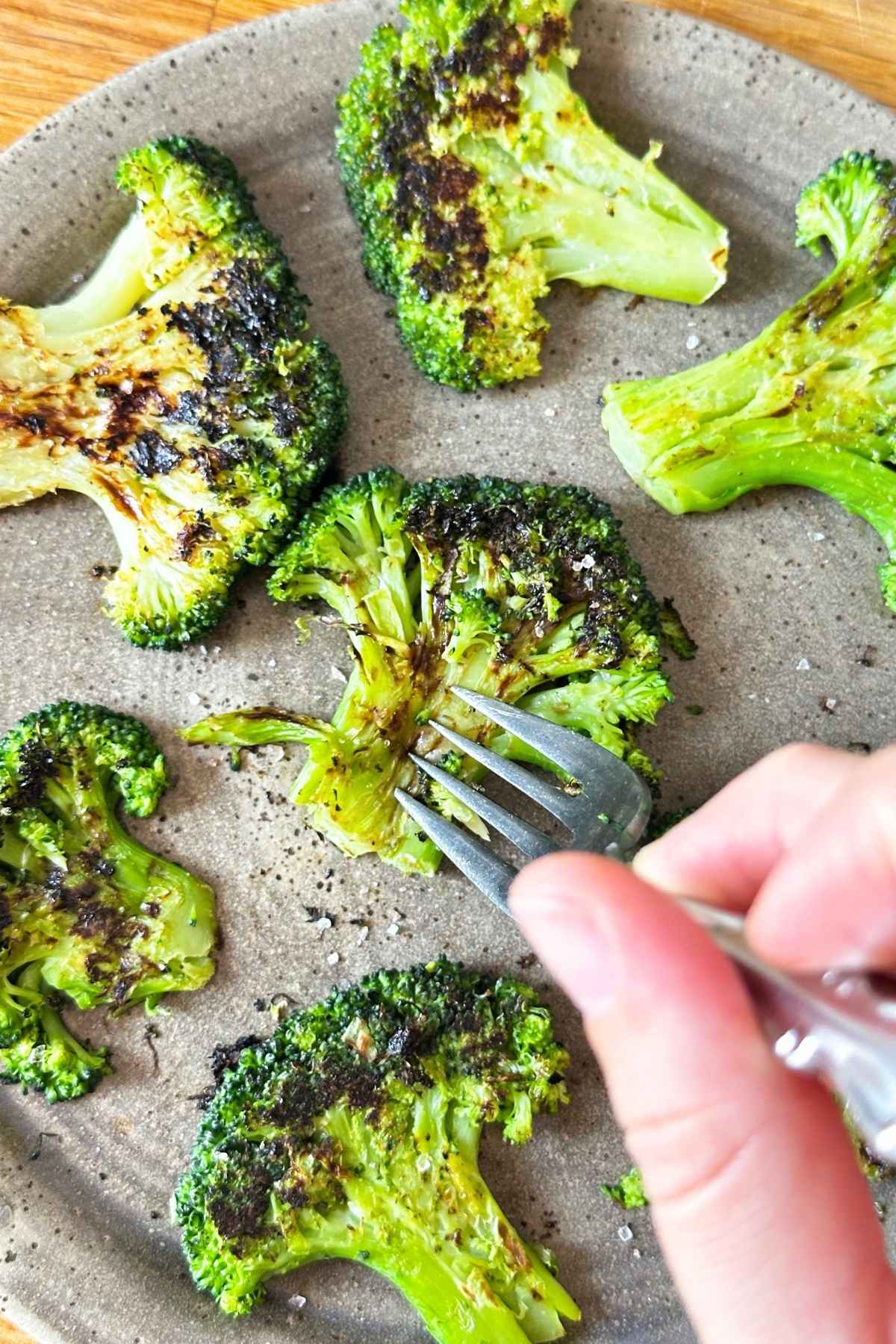 Fork poking into roasted smashed broccoli floret on a plate with little flecks of salt.