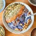 Chia pudding in a ceramic bowl topped with pumpkin seed, hemp hearts, almond butter, walnuts, and cinnamon.
