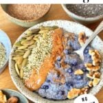 Chia pudding in a ceramic bowl topped with pumpkin seed, hemp hearts, almond butter, walnuts, and cinnamon.