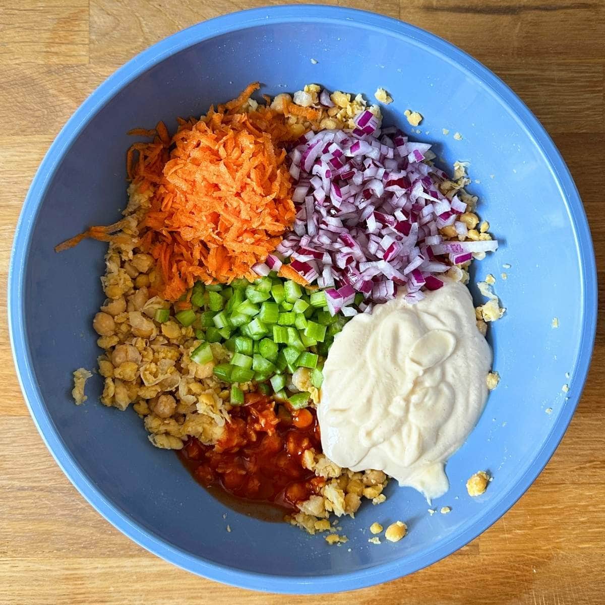 Shredded carrot, chopped onion, chopped celery, smashed chickpeas, buffalo sauce, and tofu mayo in a bowl.