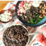 Black lentils on a spoon with a bowl lentils and a Mediterranean bowl in the background, text reads "how to cook black lentils" and "CAVA-inspired recipe".