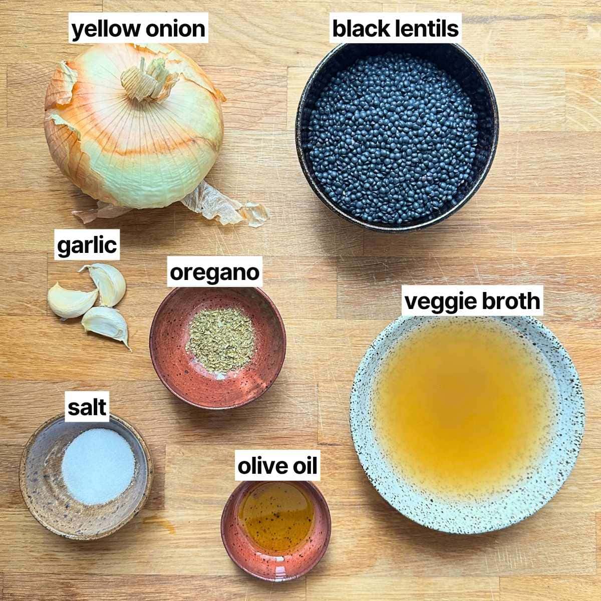 Ingredients needed to make black lentils with labels: yellow onion, black lentils, garlic, oregano, veggie broth, salt, and olive oil.