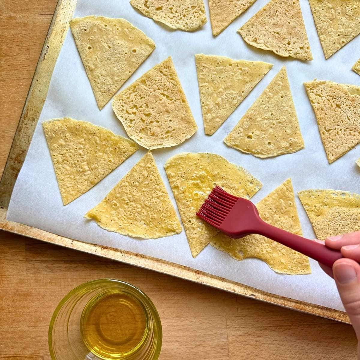 Brushing chickpea tortilla chips with olive oil before baking.