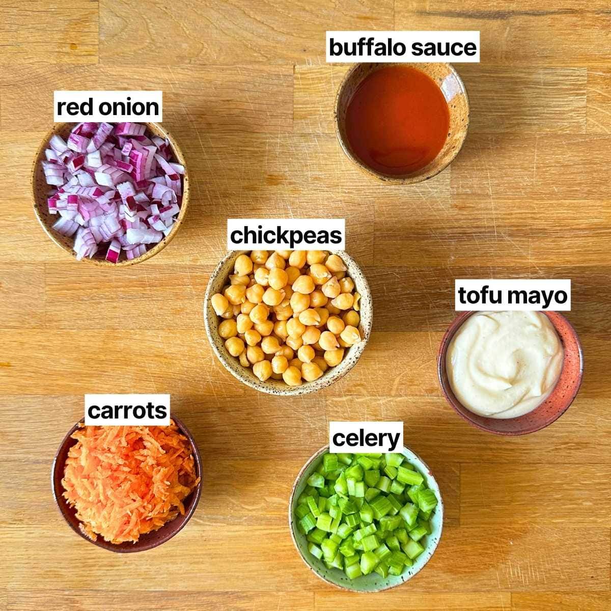Ingredients needed to make buffalo chickpea salad with labels: buffalo sauce, red onion, chickpeas, tofu mayo, carrots, and celery.