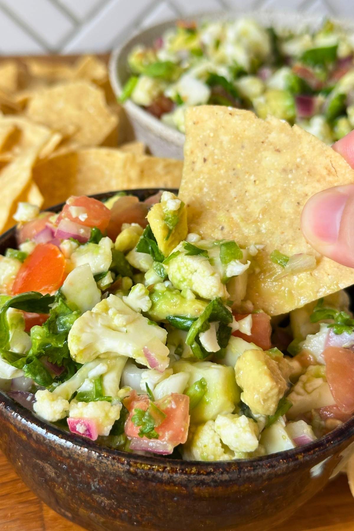 Hand dipping a corn chip into a bowl of fresh vegan cauliflower ceviche.