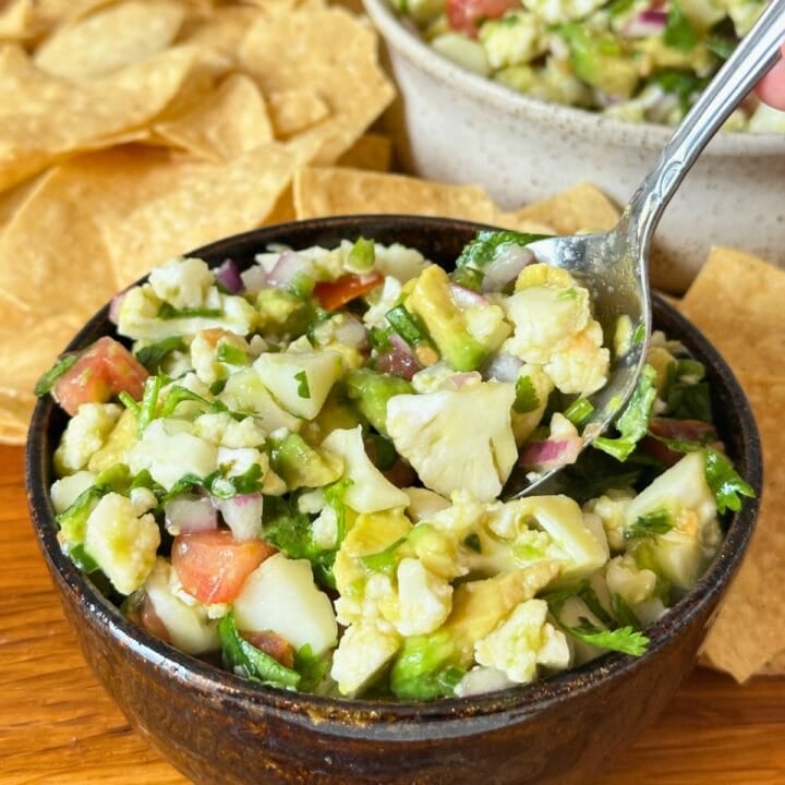 Cauliflower ceviche in a bowl with a spoon, more ceviche and corn chips are in the background.