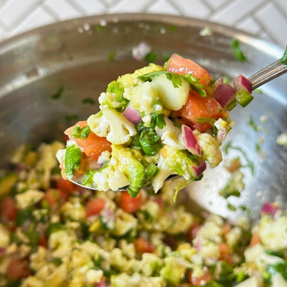 Cauliflower ceviche on a spoon with the rest of the bowl in the background.