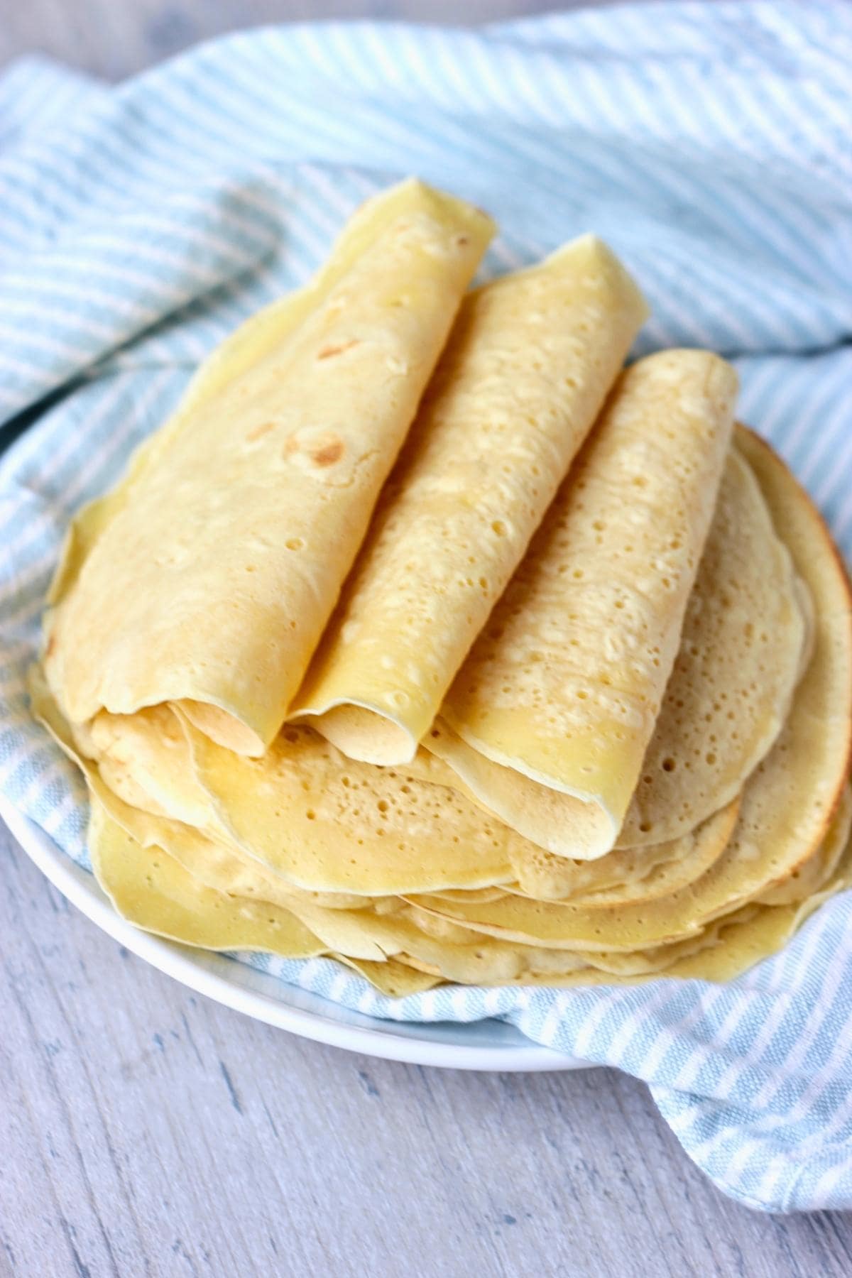 Chickpea flour tortillas stacked on a plate on top of a blue and white napkin, with 3 tortillas folded like tacos on top.