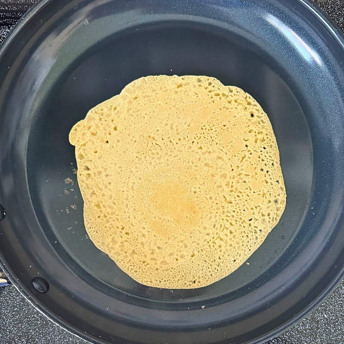 Chickpea flour tortilla cooking in a pan with little holes.
