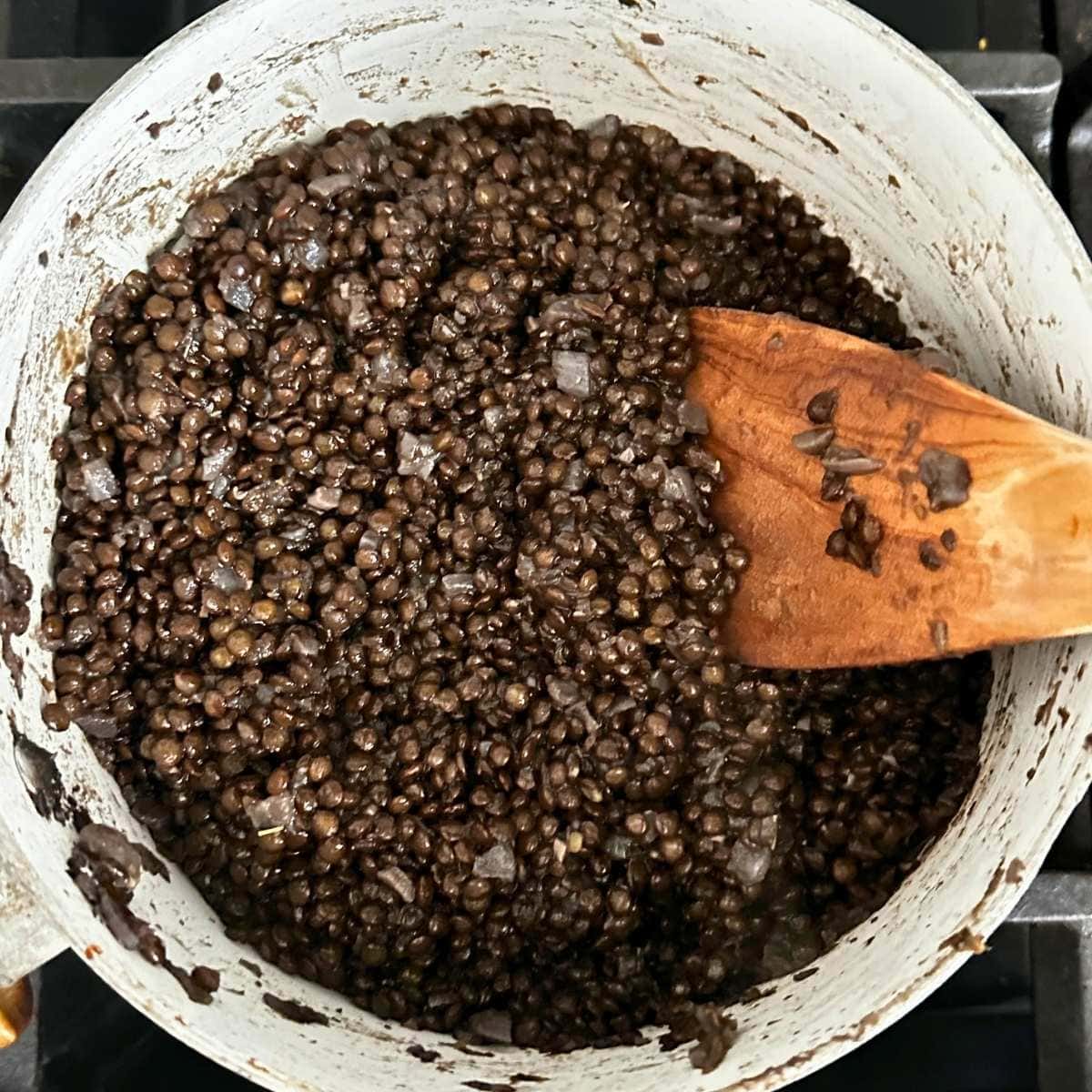 Black lentils finished cooking in a pot with all of the broth absorbed.