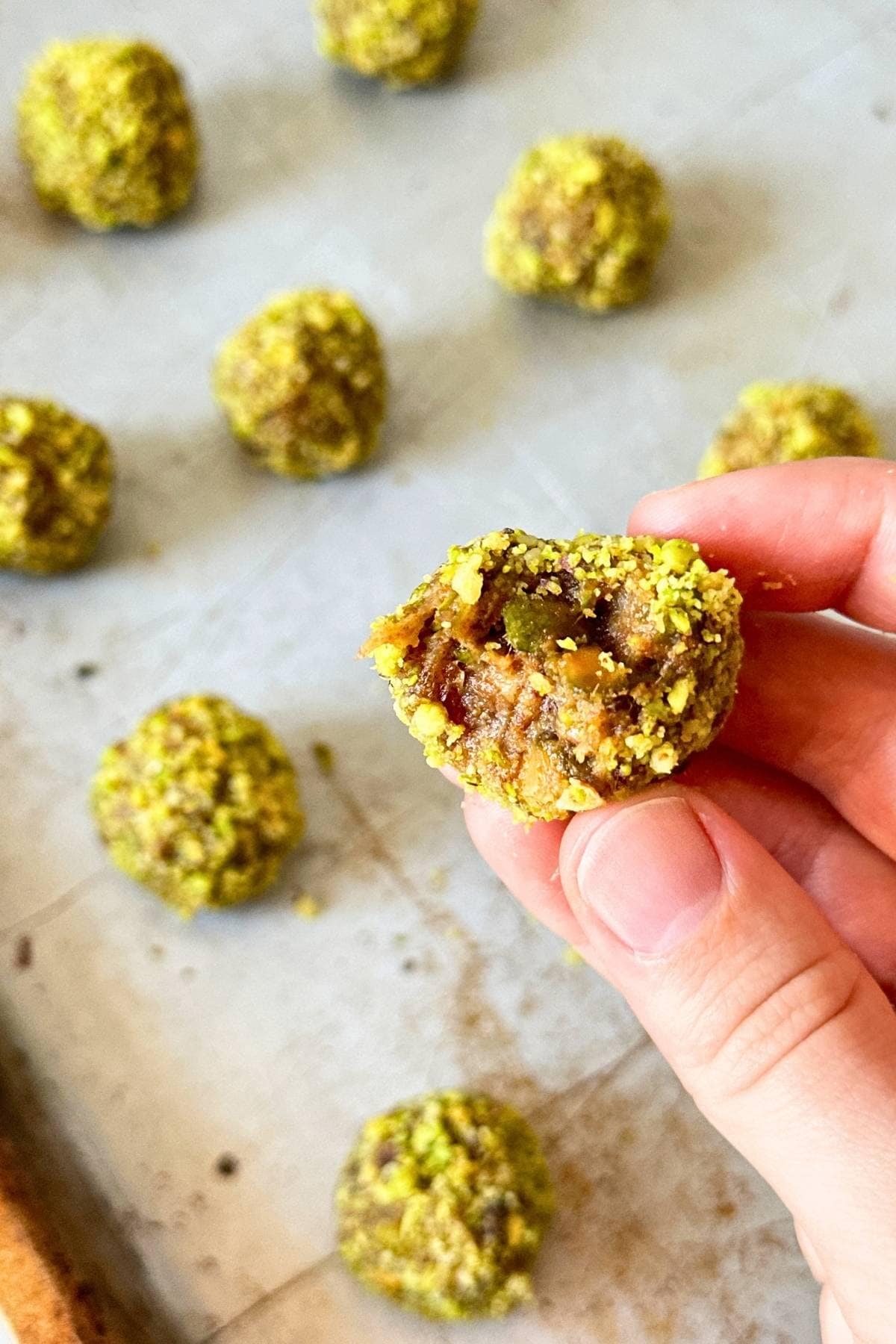Pistachio date ball with a bite taken out of it, more energy balls in the background.
