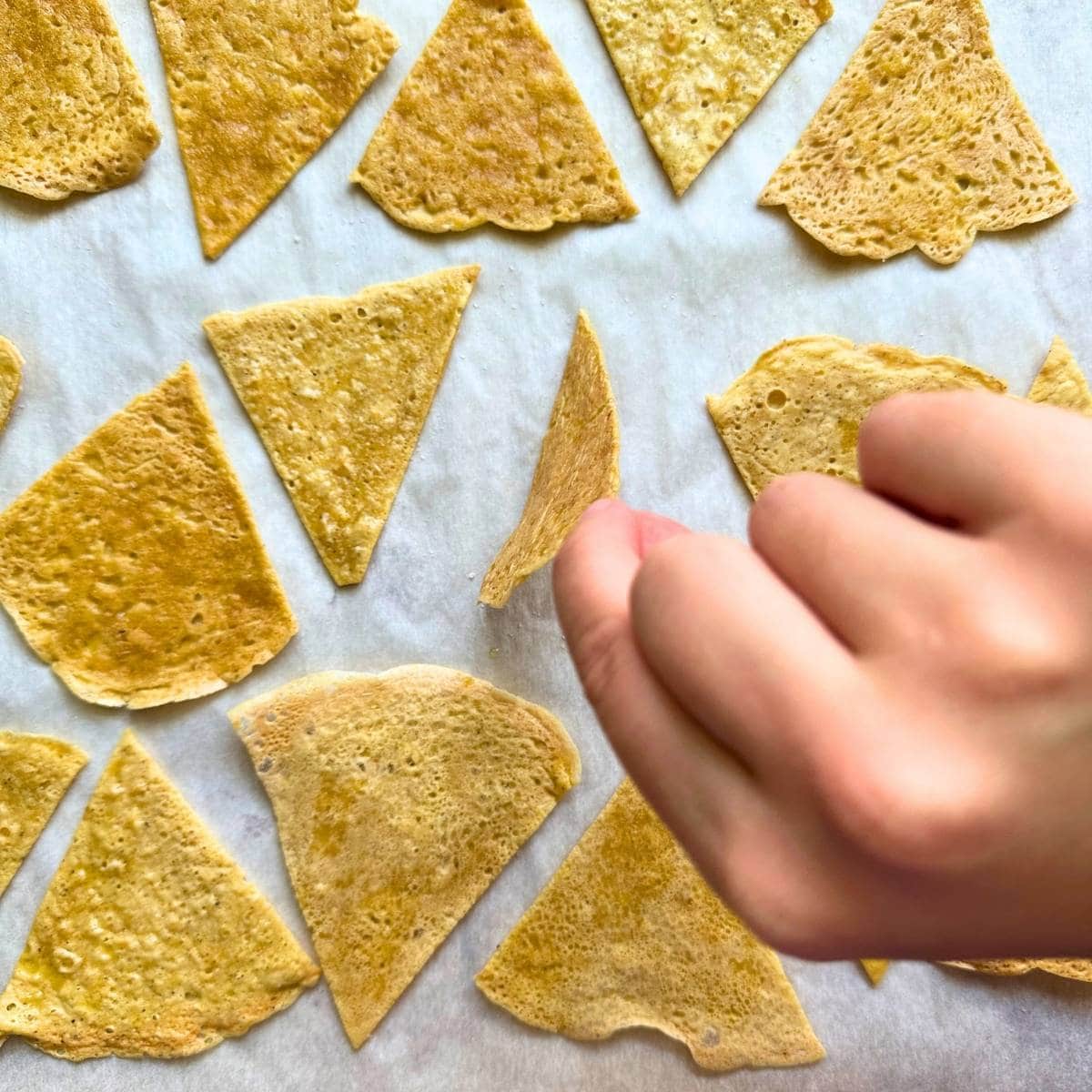 Flipping chickpea tortilla chips by hand halfway through cooking.