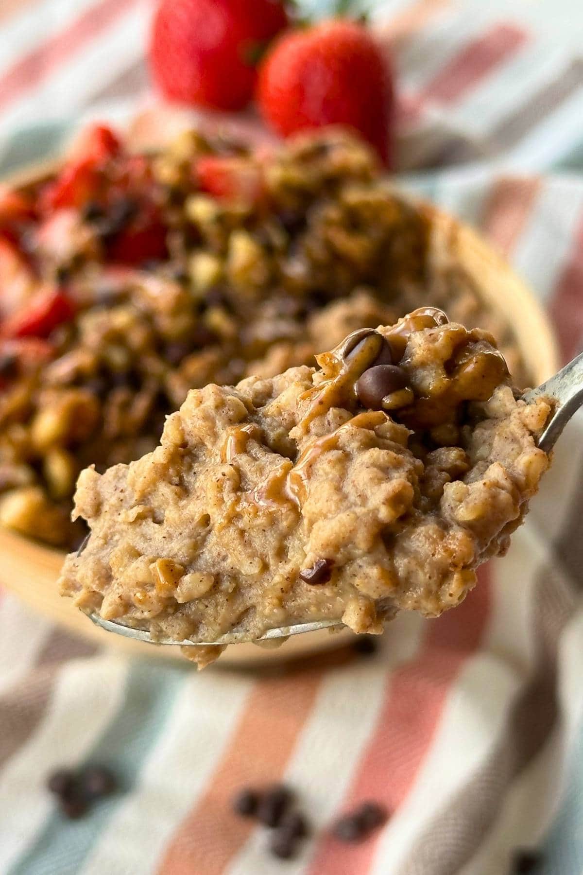 Protein steel cut oatmeal on a spoon with chocolate chips and almond butter, more oatmeal is in the background.