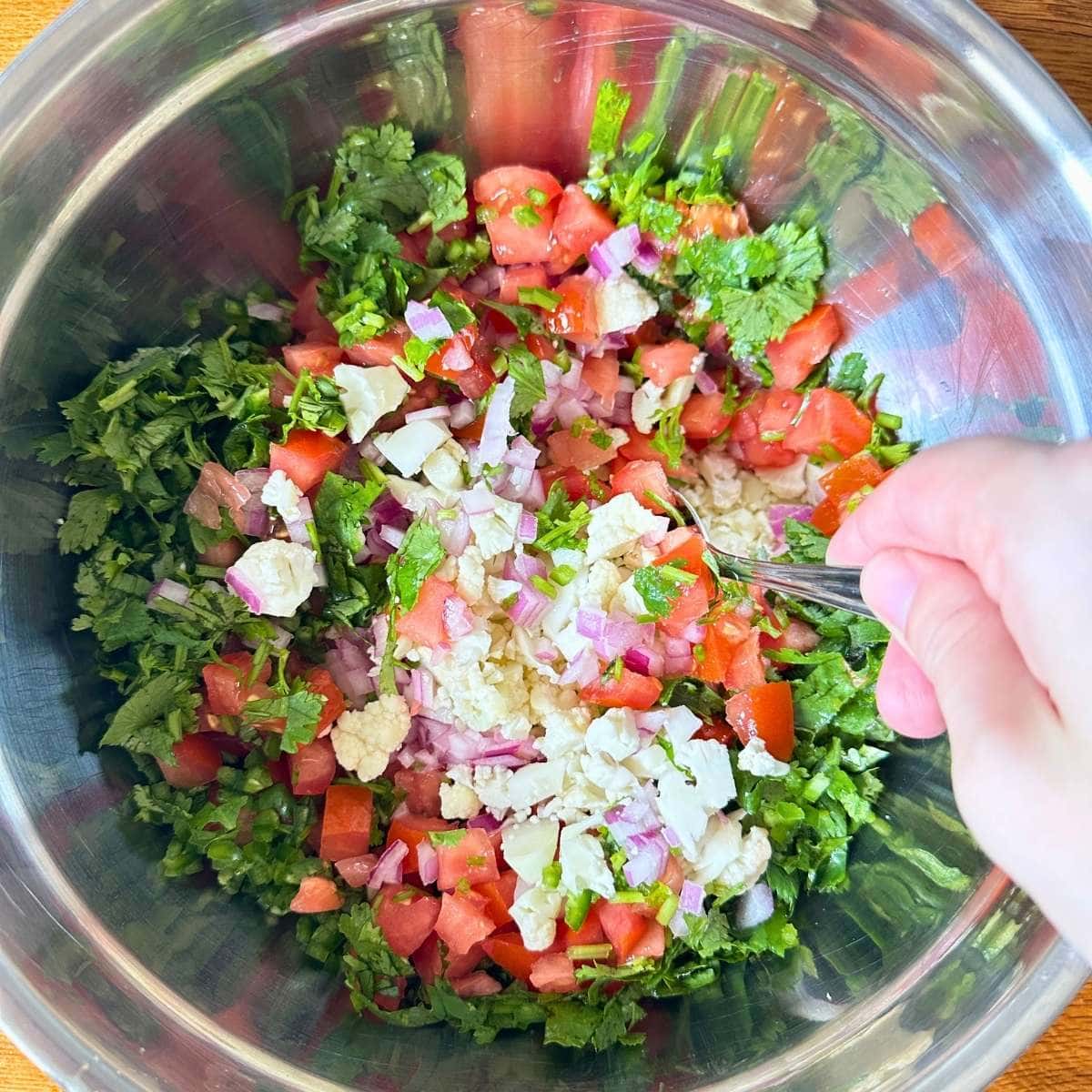 Cauliflower, cilantro, tomato, and onion all combined in a metal bowl.