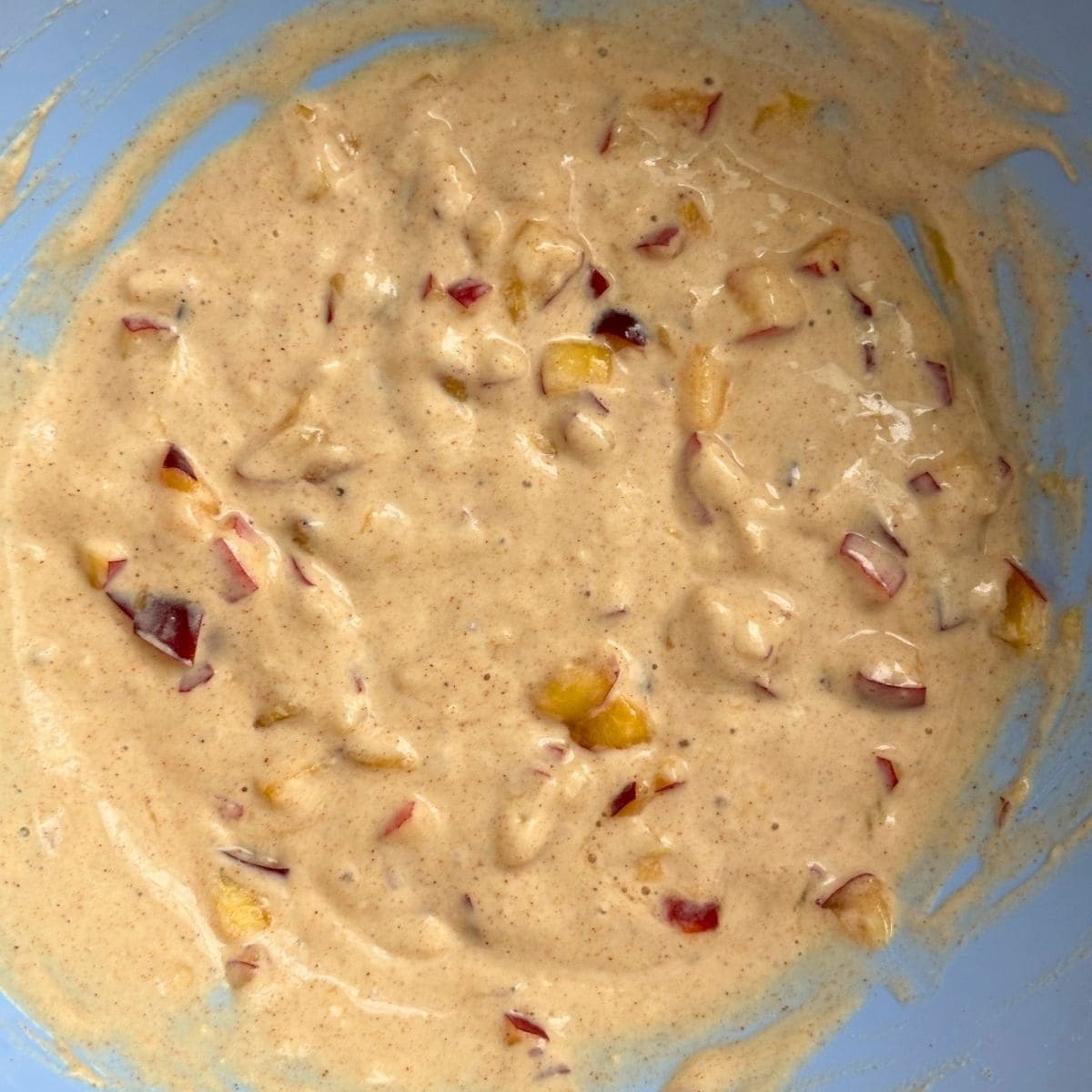 Summer fruit pancake batter in a bowl with chunks of peaches throughout.