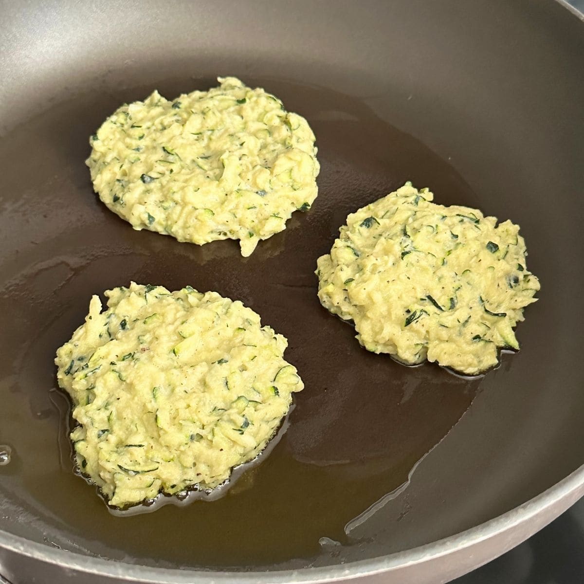 Cooking zucchini fritters in a pan with oil.