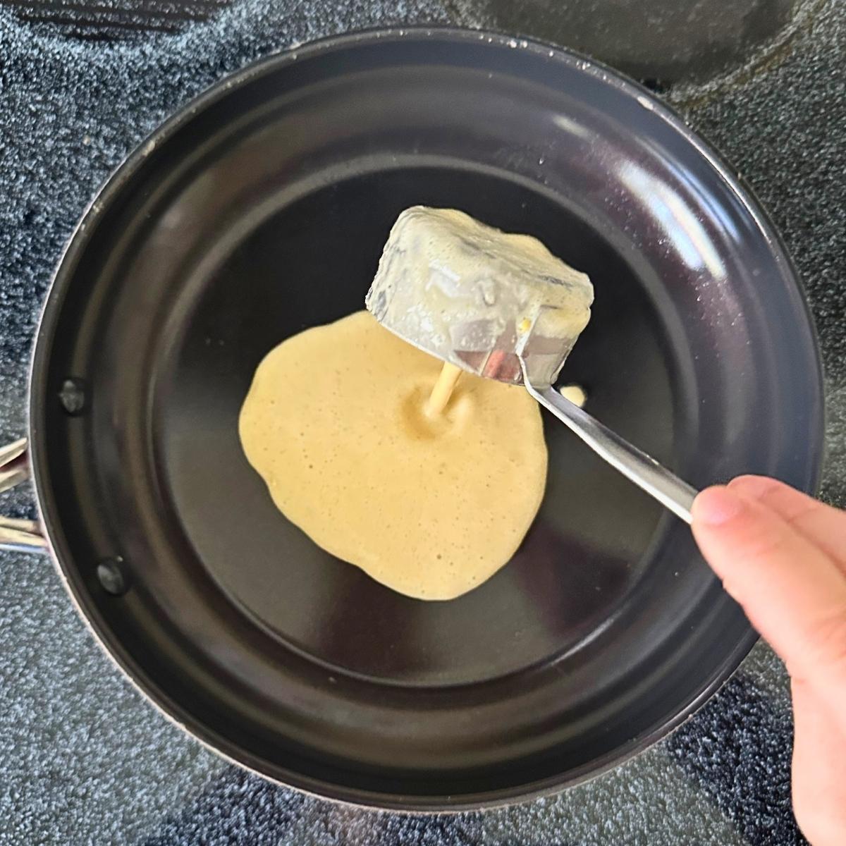 Pouring chickpea tortilla batter into a pan on the stovetop.