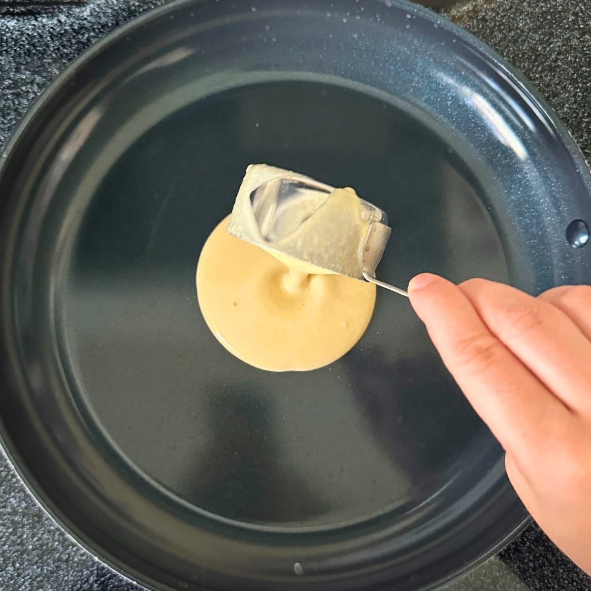 Using a measuring cup to pour chickpea tortilla batter into a pan.