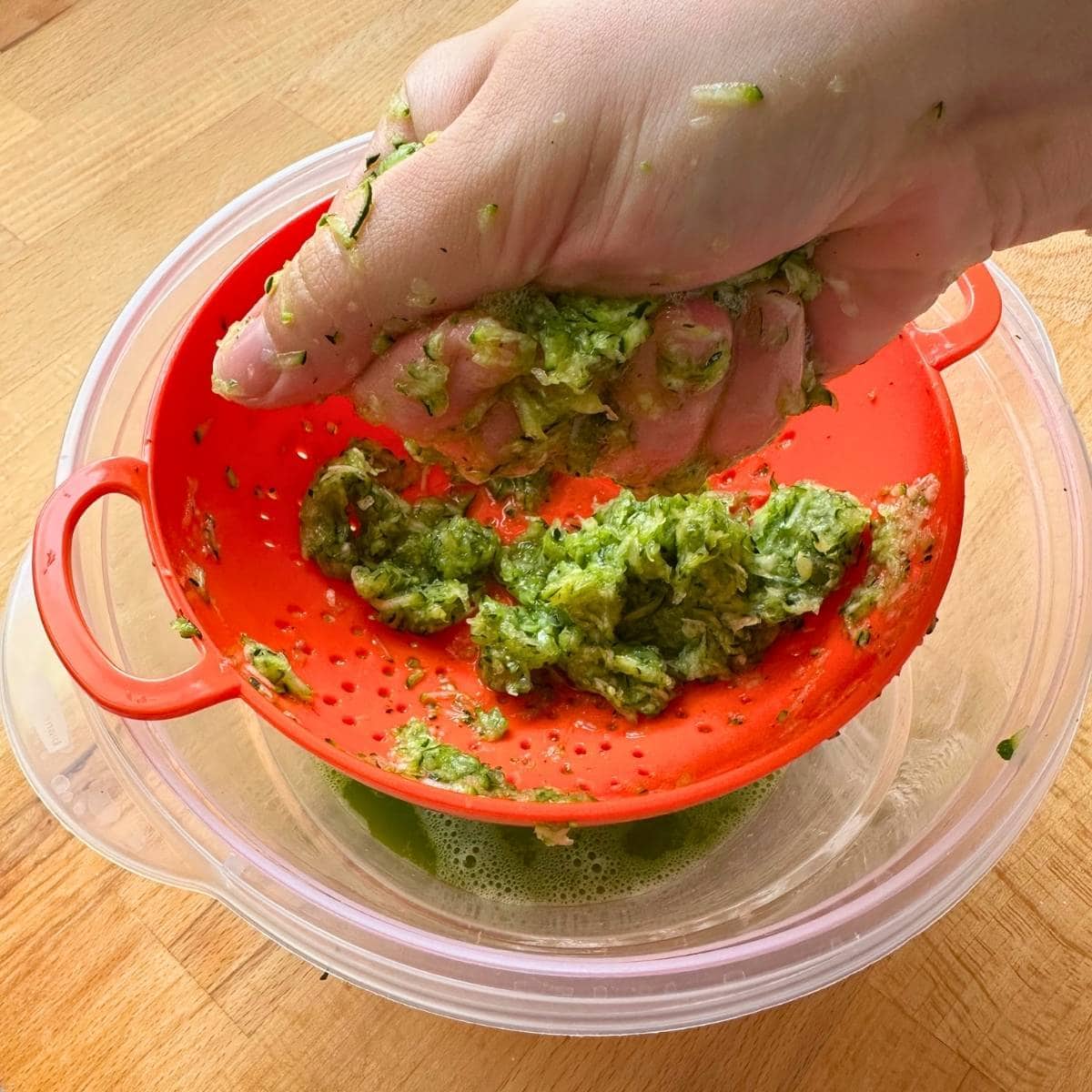 Pressing shredded zucchini by hand over a colander.