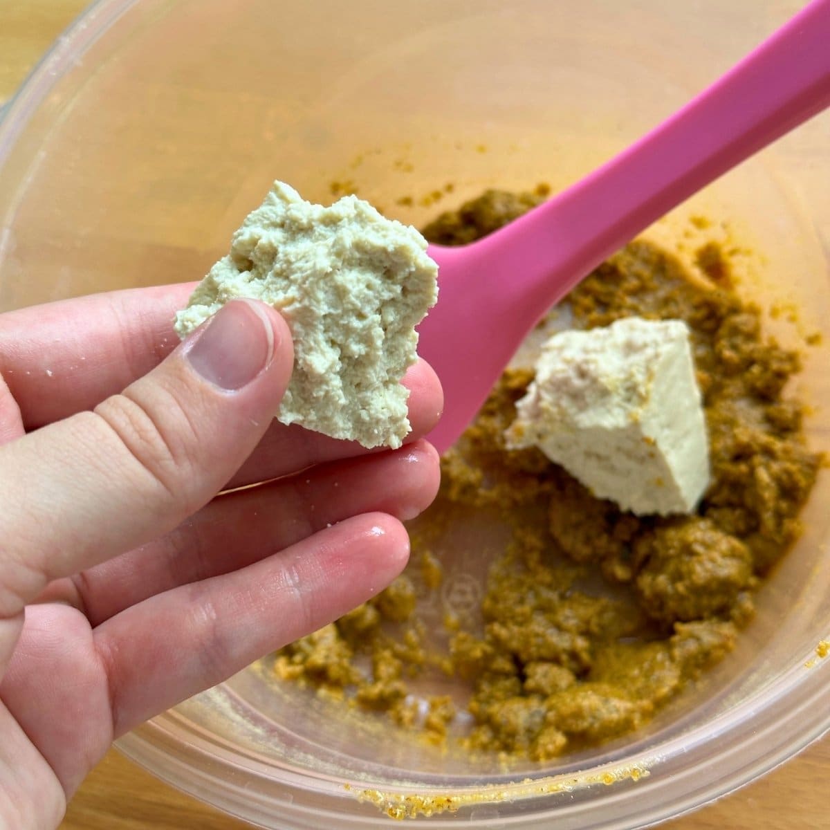 Breaking the block of tofu apart by hand into smaller bite-sized pieces.