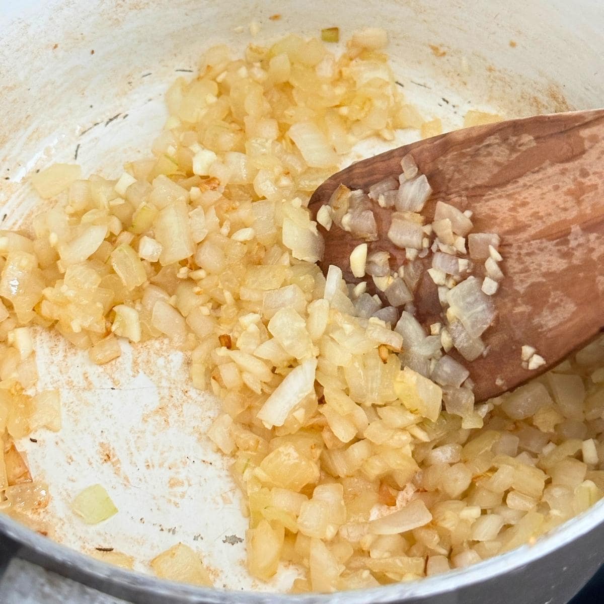 Sautéing onion and garlic in a pot and mixing with a wooden spatula.
